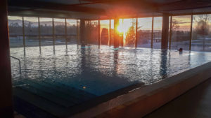 Hallen-Schwimmbecken mit verglasten Hallenwänden und Sonnenuntergang