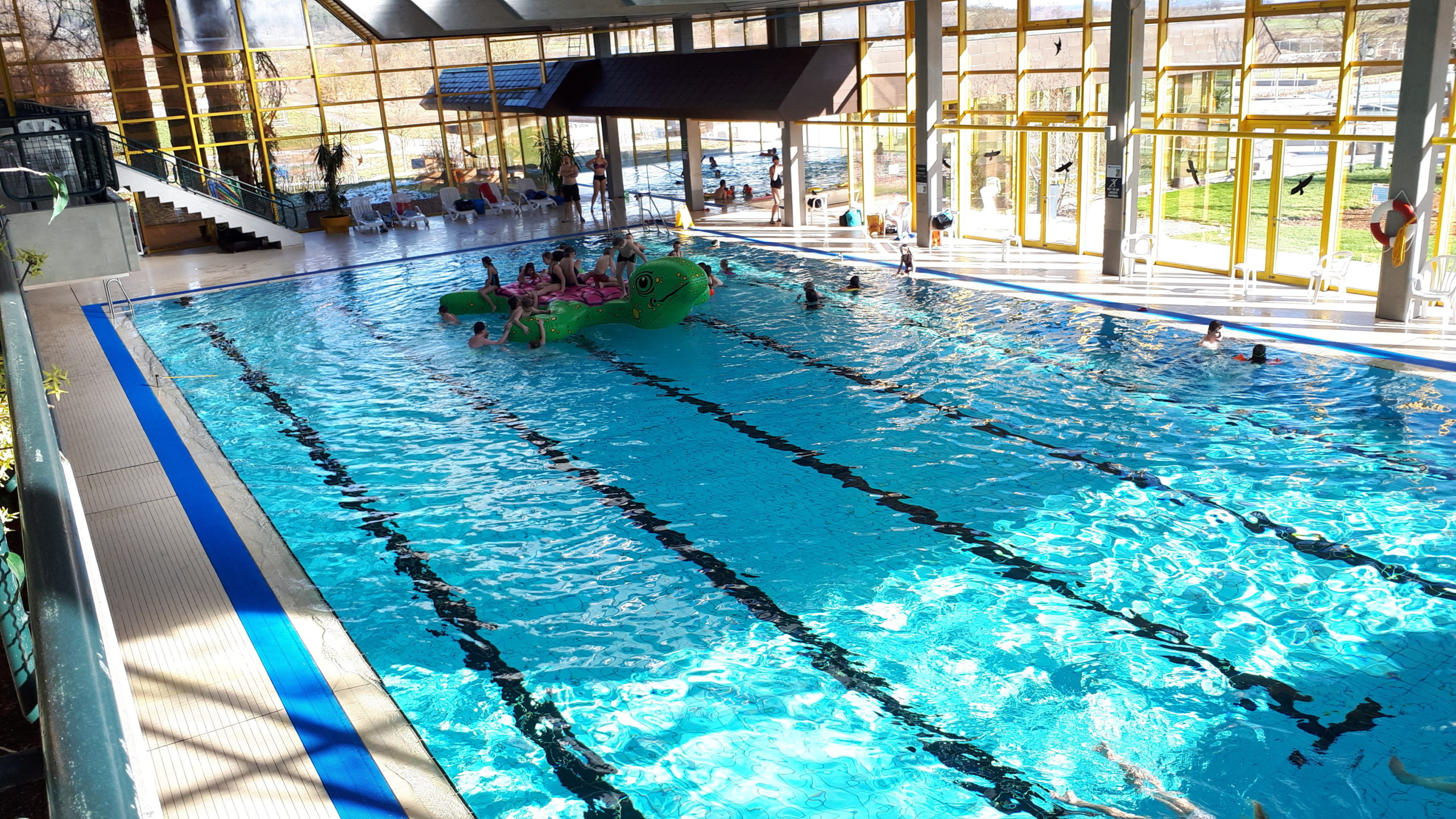 Hallen-Schwimmbecken mit mehreren Schwimmern, Startblock mit gesperrt-Schild und verglaste Hallenwänden in der Dämmerung